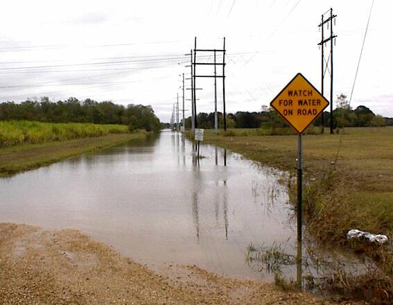 Strae mit Warnschild steht unter Wasser.